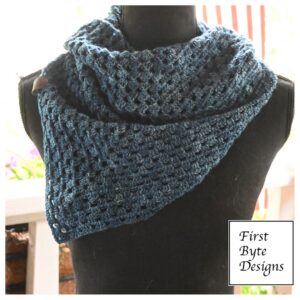 blue-grey crocheted triangle scarf or shawl is displayed on a black mannequin torso against a brightly lit background. The scarf features an open, mesh-like granny stitch pattern and is draped loosely around the neck, with one pointed end hanging down the front. In the bottom right corner, a white square logo with a black border contains the text "First Byte Designs"